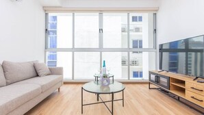 Ein modernes Wohnzimmer mit einer Couch, einem Glastisch, einer TV-Konsole und einem großen Fenster mit Blick auf die Stadt.