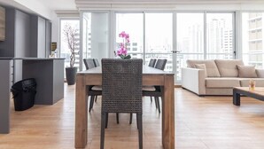 Ein modernes Wohnzimmer mit Essbereich, großen Fenstern und Blick auf hohe Gebäude.