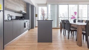 Eine moderne Küche mit grauen Schränken, einer zentralen Kochinsel und einem Essbereich mit Korbstühlen.