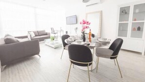 A modern living room with a grey sofa, a dining table with chairs, and a TV mounted on the wall. - Luxury 2 bedroom apt free parking and Pool (Panamá)