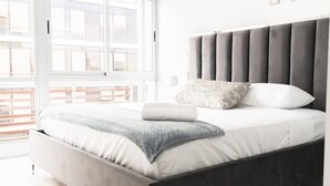 A modern bedroom with a large bed, a grey headboard, and a window with blinds. - Luxury 2 bedroom apt free parking and Pool (Panamá)