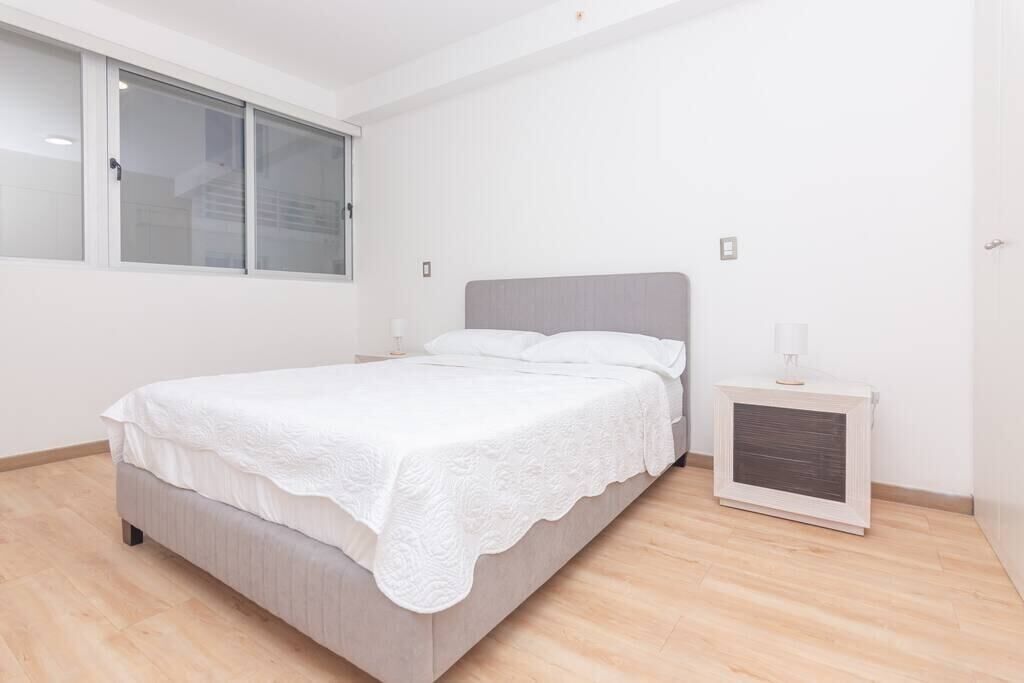 A bedroom with a bed, a nightstand, a window, and a radiator.