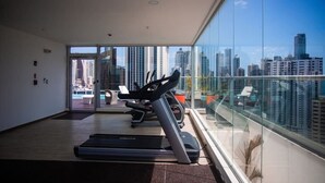 A gym with treadmills and exercise equipment, large windows with a city view, and a modern interior design.