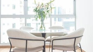 Un comedor con una mesa redonda, cuatro sillas, una lámpara colgante y una ventana con vista a la ciudad.