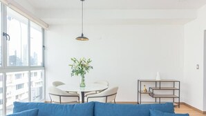 Un salon moderne avec un canapé bleu, une table à manger avec des chaises, une plante en pot et une étagère en métal noir.