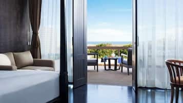 A modern hotel room with a large bed, a balcony with a table and chairs, and a view of the ocean.