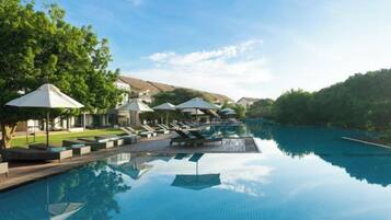 A clear swimming pool with lounge chairs and umbrellas, surrounded by trees and hills.