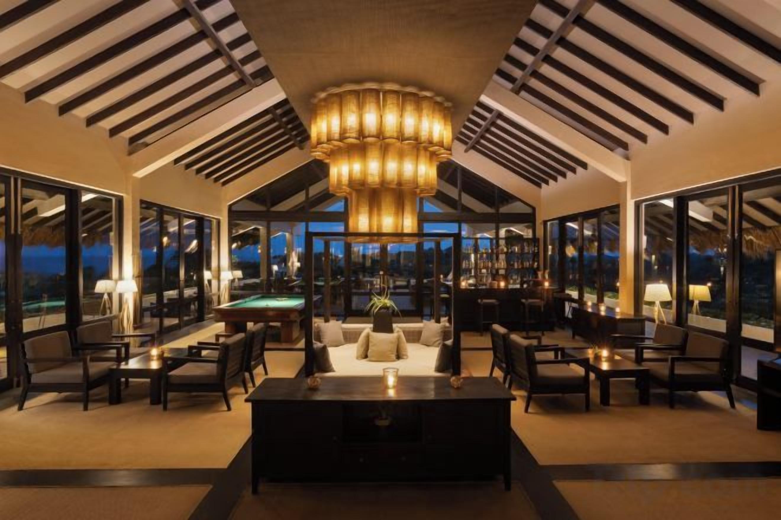 A spacious lounge area with a pool table, comfortable seating, and large windows offering a view of the night sky.