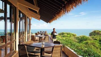 An outdoor dining area with tables and chairs, overlooking a coastal landscape.