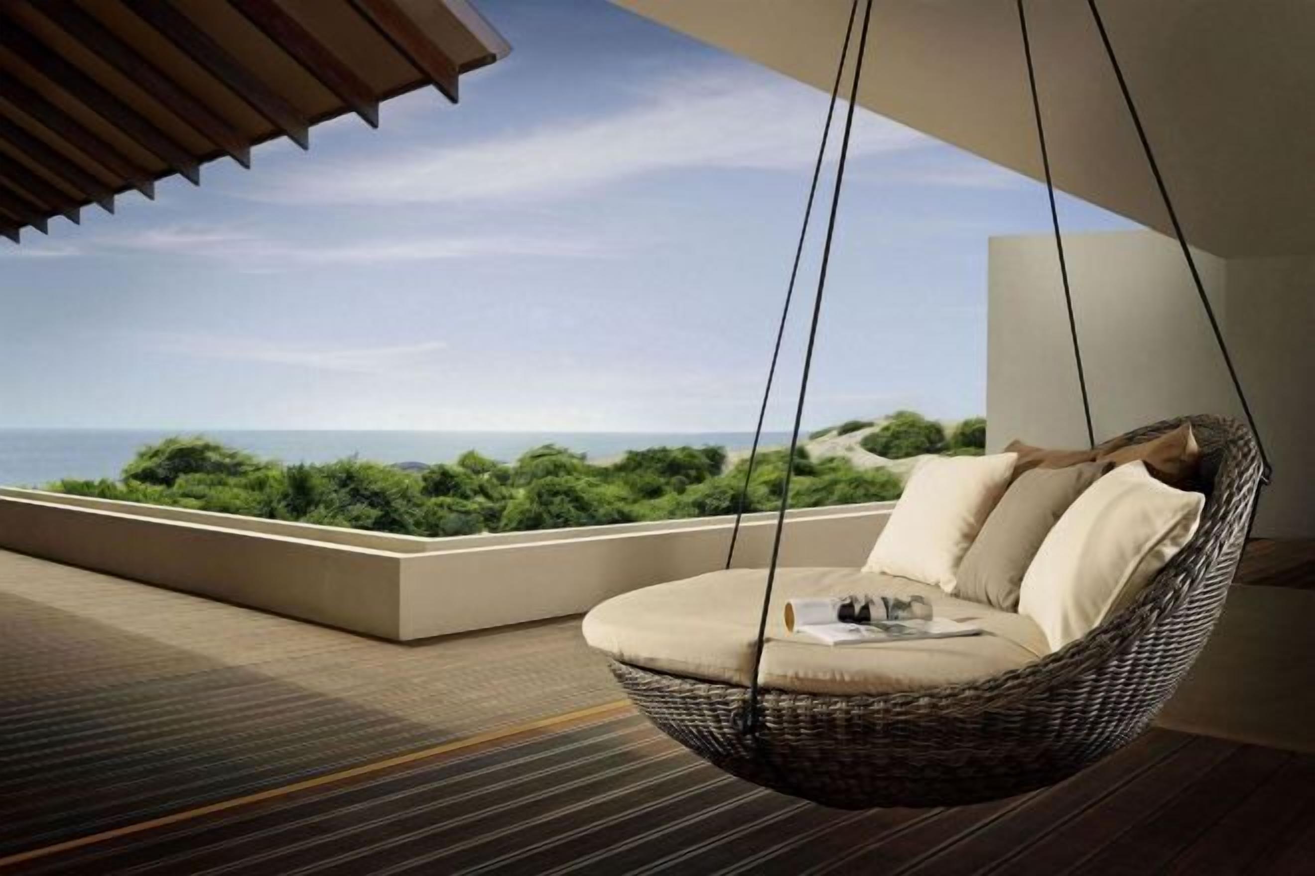 A hanging chair with cushions on a balcony overlooking a sea view.