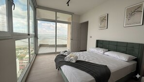 A bedroom with a large bed, a view of the city through floor-to-ceiling windows, and two framed pictures on the wall.