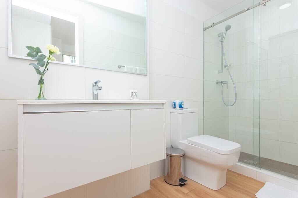 A modern bathroom with a glass shower enclosure, a white toilet, and a sink with a mirror above.