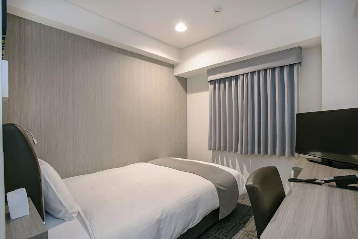 Habitación de hotel con dos camas, un escritorio, una silla, un televisor y una ventana con cortinas.