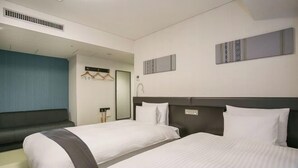 Ein Hotelzimmer mit zwei Betten, einem Spiegel, einem Kleiderschrank und einem kleinen Badezimmer.
