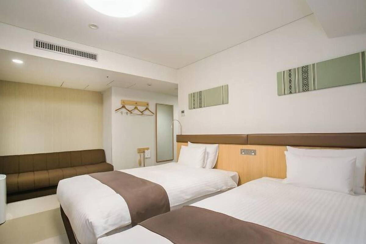Habitación de hotel con dos camas, un sofá, un espejo y una lámpara de pared.
