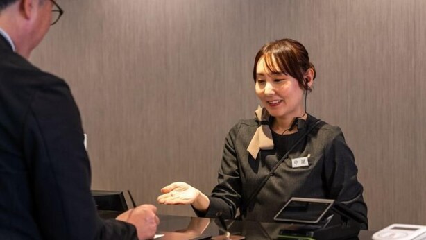 Ein Hotelrezeptionstresen mit einem Tablet, einer Waage und einem Namensschild am Mitarbeiter.