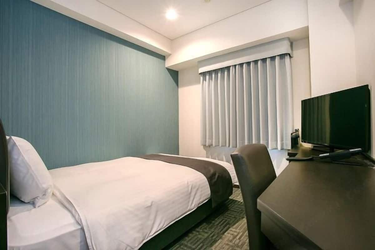 Habitación de hotel con dos camas, un escritorio, una silla, un televisor y una ventana con cortinas.