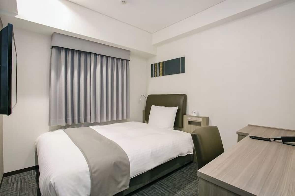 Habitación de hotel con cama, escritorio, silla, mesita de noche y ventana con cortinas.