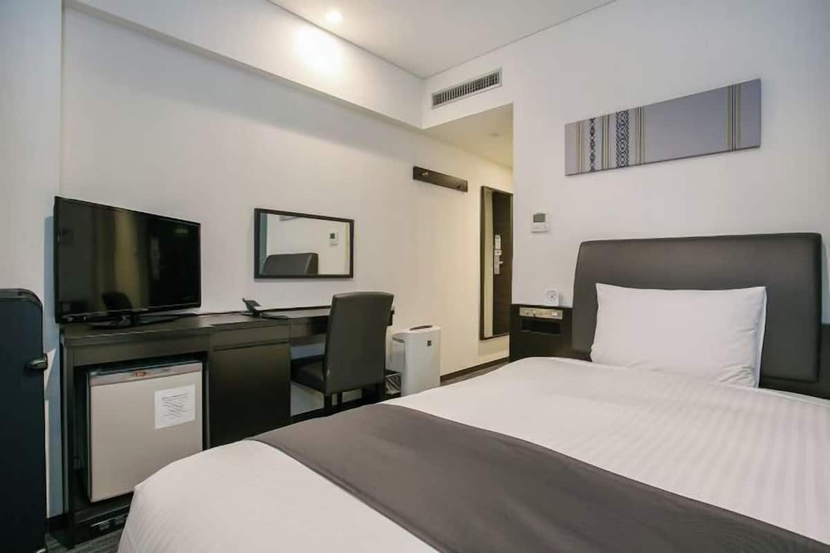 Una habitación de hotel con una cama, un escritorio con computadora, televisor y un refrigerador pequeño.