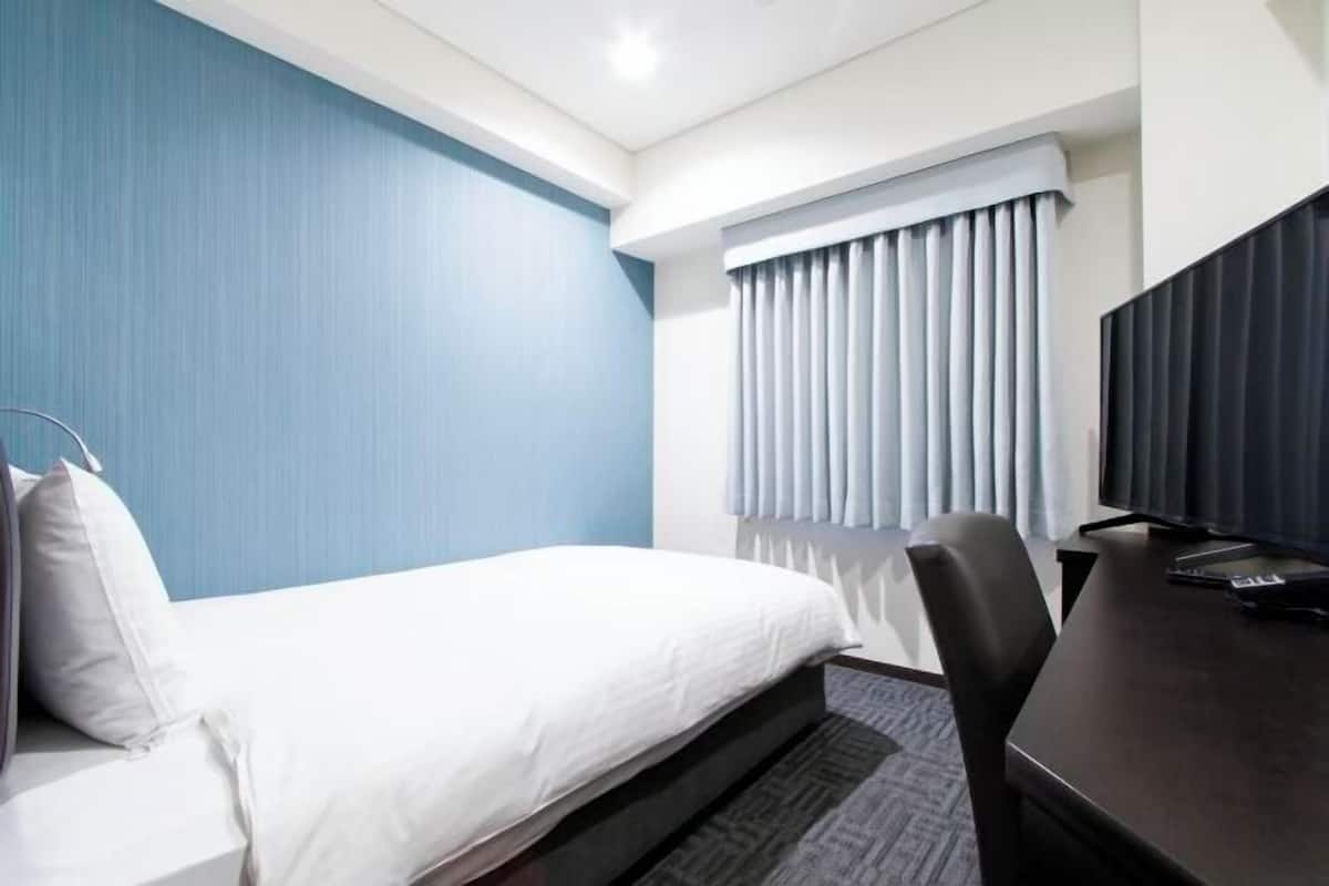 Habitación de hotel con cama, escritorio, silla, televisión y ventana con cortinas.