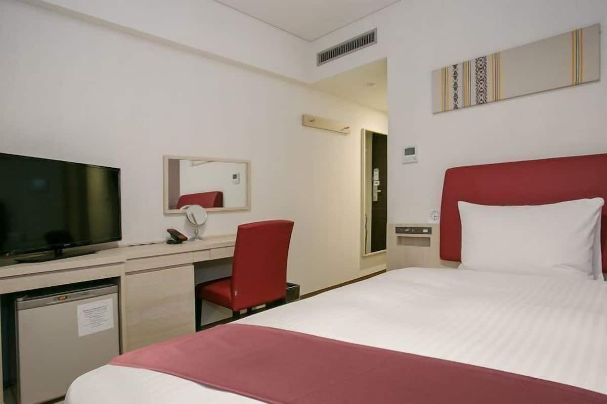 Habitación de hotel con cama, escritorio con computadora, televisor, una silla roja y cabecera roja.