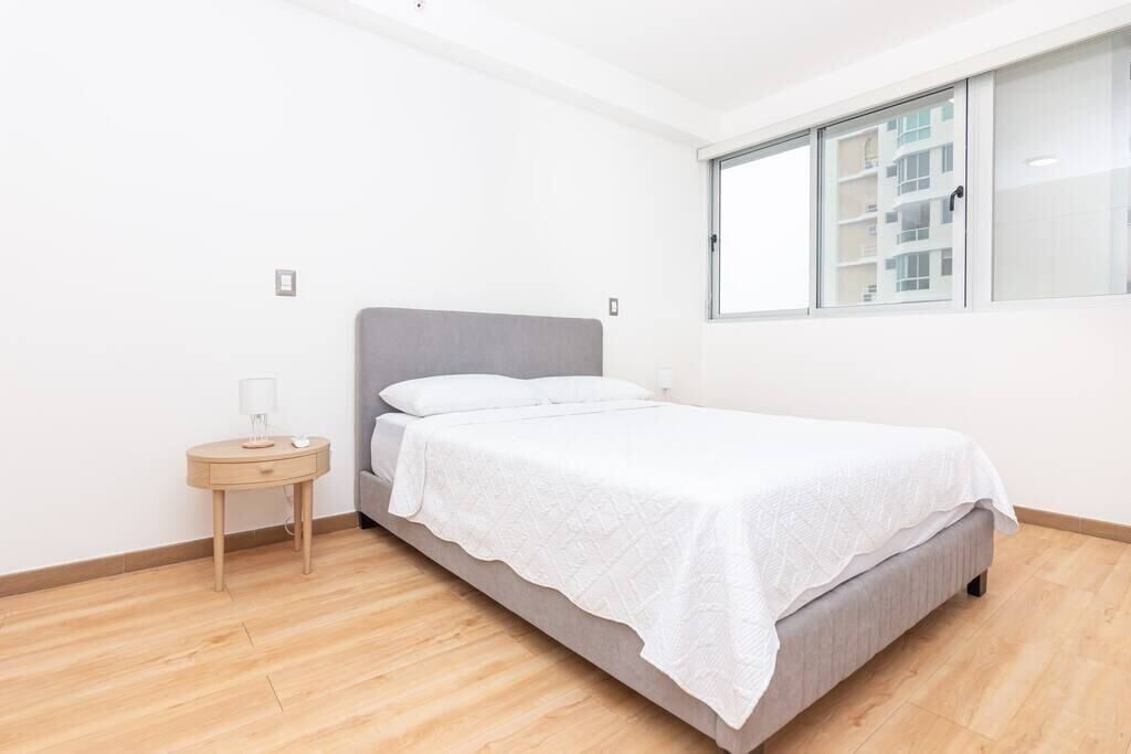A bedroom with a bed, a bedside table, and a window.