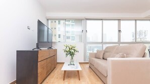 A modern living room with a flat-screen TV, a wooden cabinet, a beige sofa, and a coffee table with a vase of flowers. - Luxury 1 bedroom apt with free parking (Panamá)