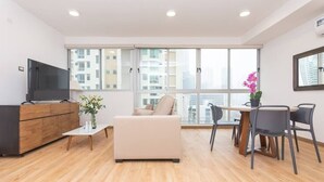 A modern living room with a sofa, a dining table with chairs, a TV on a wooden cabinet, and a large window with a city view. - Luxury 1 bedroom apt with free parking (Panamá)