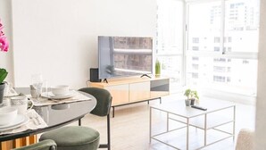 Una sala de estar moderna con comedor, un televisor de pantalla plana, un mueble de madera y un ventanal con vistas a la ciudad.
