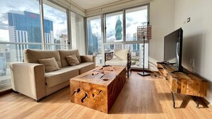 A modern living room with a large window, a sofa, a coffee table, a TV, and a wooden side table.