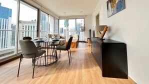 A modern living room with a dining area, large windows, and a city view.