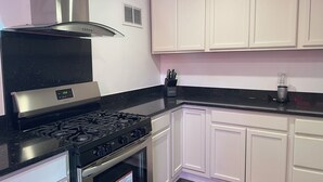Una cucina con mobili bianchi, un piano di lavoro nero, elettrodomestici in acciaio inossidabile e una cappa sopra il fornello.