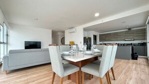 A modern living room with a grey sofa, a dining table set for four, and a kitchen in the background.