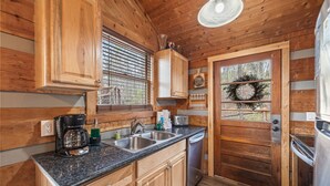 A wooden cabin kitchen with a granite countertop, stainless steel sink, and a built-in dishwasher. - You need a Time Out on Your Next Getaway? (Sevierville)