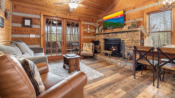A cozy log cabin interior with a fireplace, leather furniture, and a large window. - You need a Time Out on Your Next Getaway? (Sevierville)