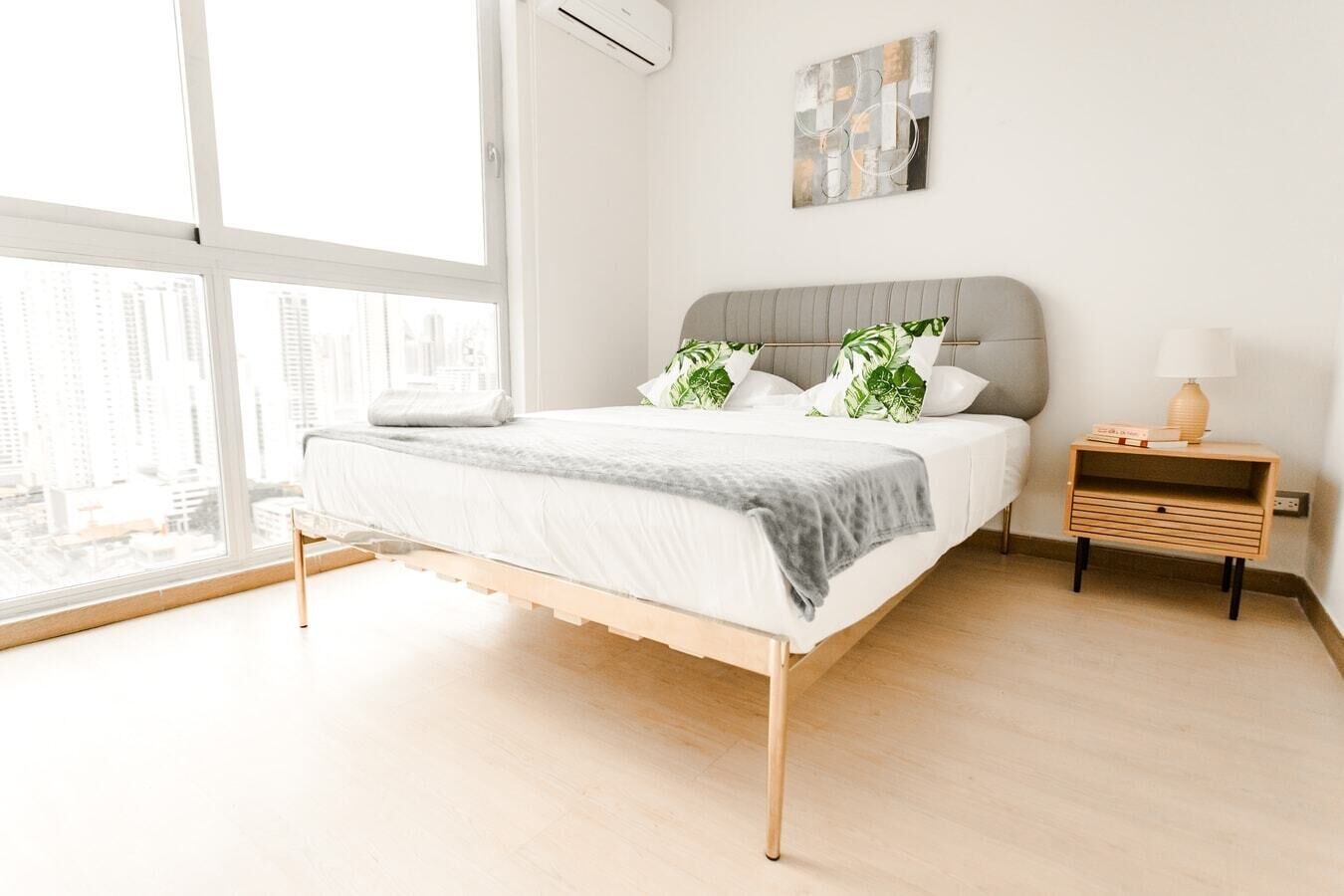 Ein modernes Schlafzimmer mit Bett, Nachttisch und Blick auf die Stadt durch große Fenster.