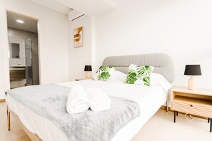 Ein modernes Schlafzimmer mit einem großen Bett, zwei Nachttischen mit Lampen, einer Wand-Klimaanlage und einer Tür zu einem Badezimmer.