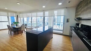 Una cocina moderna con una isla grande, comedor con sillas y ventanas amplias con vista a la ciudad.