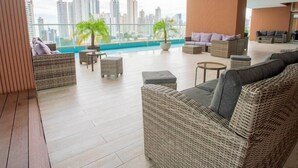 A modern lounge with wicker furniture, a glass railing, and a view of city buildings.