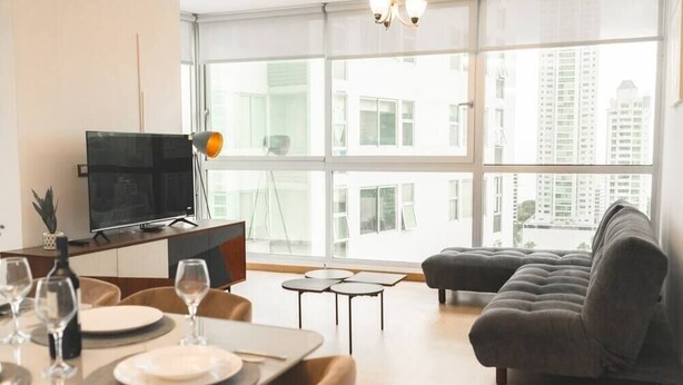 A modern living room with a dining area, large windows, a sofa, and a TV.