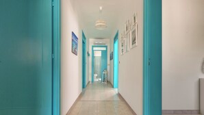 A hallway with teal-colored doors and walls, leading to a room with a toilet and a decorative lamp. - Villa Mormora by BarbarHouse (Padula Fede)