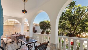 A covered patio with a table and chairs, potted plants, and a view of a tree.