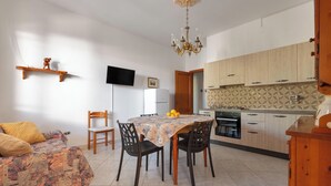 A modern kitchen with wooden cabinets, a dining table with chairs, a chandelier, and a flat-screen TV mounted on the wall.
