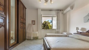 A hotel room with a large bed, a wardrobe, a window with a view of trees, and a ceiling fan.