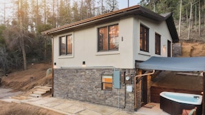 A two-story house with a stone exterior, a hot tub, and a covered patio area. - Bungalow w/ Relaxing Private Hot Tub, Scenic Mountain Views (Cascade-Chipita Park)