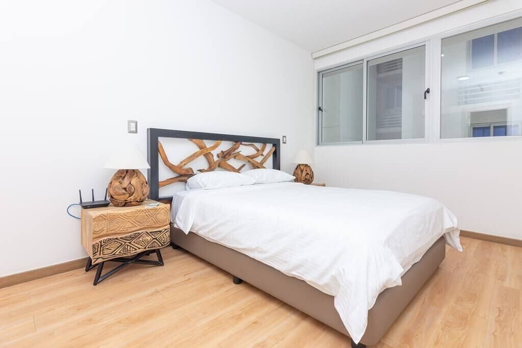 A bedroom with a bed, a nightstand, a decorative wall piece, and a window.
