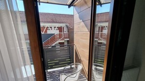 A balcony with a metal chair, a glass door, and a view of a building with a tiled roof. - Apartment Martinus-r (Sveti Martin na Muri)