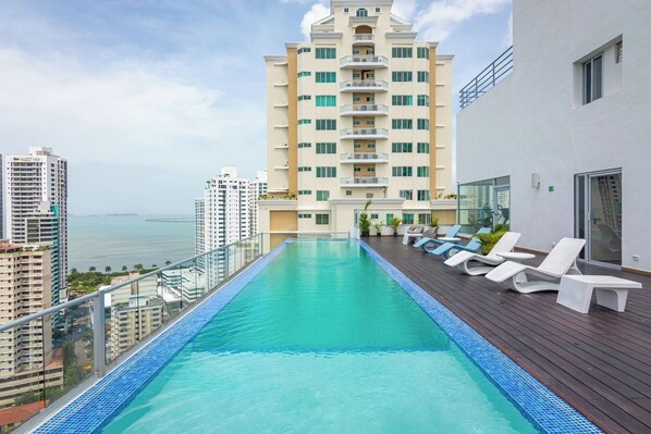 A rooftop infinity pool with white lounge chairs and a view of the ocean.