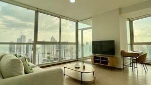 A spacious living room with a large window, a sofa, a coffee table, a TV, and a desk.