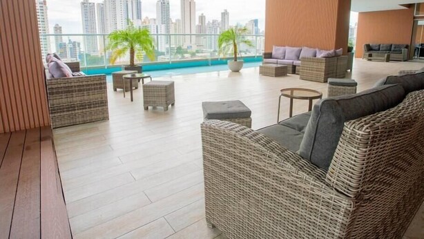 A modern lounge with wicker furniture, a glass railing, and a view of city buildings.